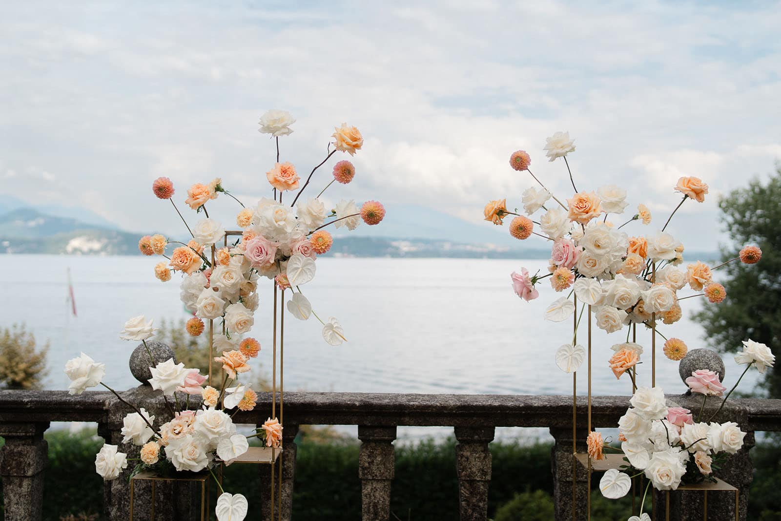 Foto di un allestimento floreale per matrimoni, con fiori dai toni del pesca e dell'arancio chiaro, realizzato vicino alle sponde di un lago.