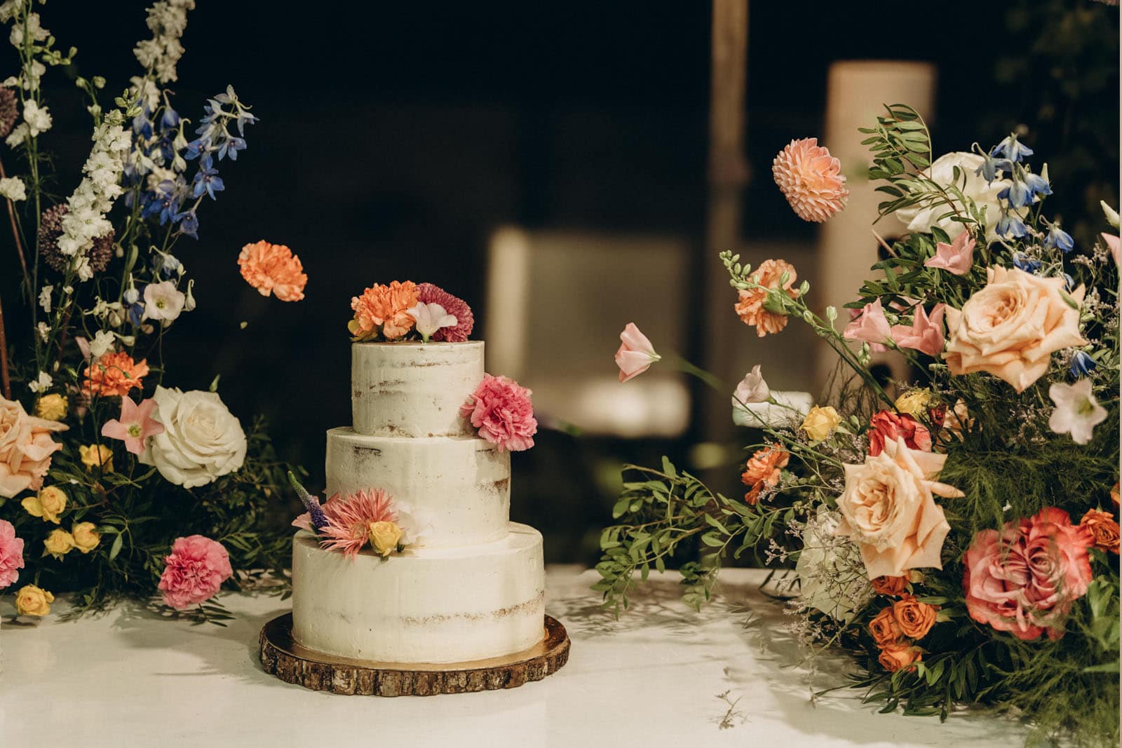 Allestimento floreale da tavolo realizzato per un evento. I fiori, dai colori rosa e arancio, sono stati utilizzati sia nella realizzazione di centro tavola e segna posti, sia per decorare una torta a tre strati di colore bianco.